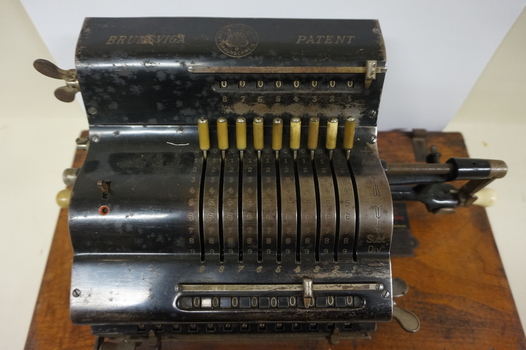 Black register shaped object on wooden board with metal levels and handles.