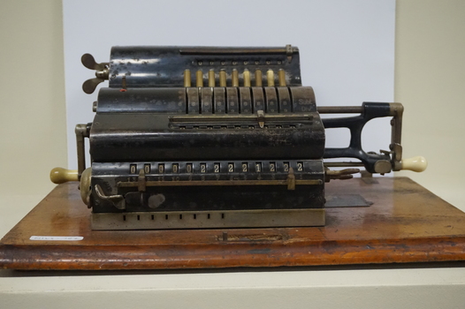 Black register shaped object on wooden board with metal levels and handles.