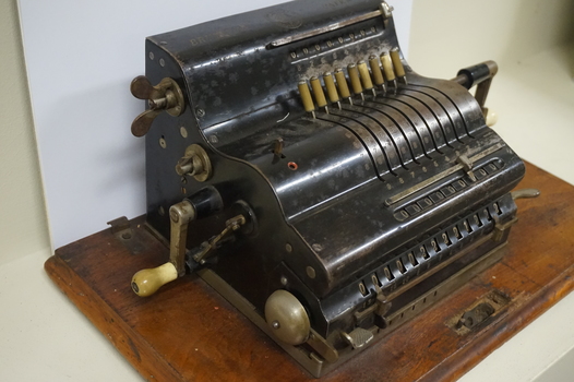 Black register shaped object on wooden board with metal levels and handles.