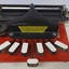 Metal braille machine with red base and 7 white wood keys