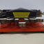 Metal braille machine with red base and 7 white wood keys