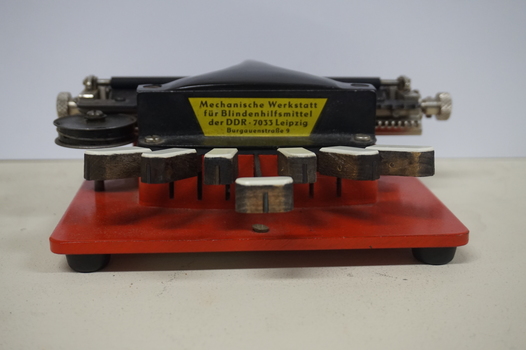 Metal braille machine with red base and 7 white wood keys