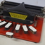 Metal braille machine with red base and 7 white wood keys