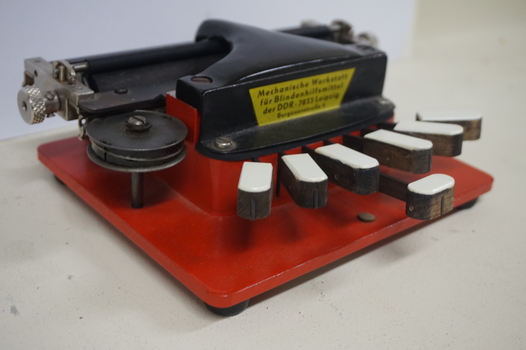 Metal braille machine with red base and 7 white wood keys
