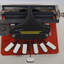 Metal braille machine with red base and 7 white wood keys