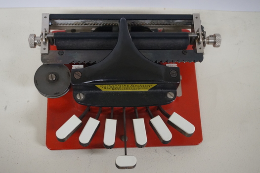 Metal braille machine with red base and 7 white wood keys