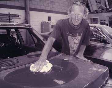 Man smiling at camera as he wipes dust from a car bonnet