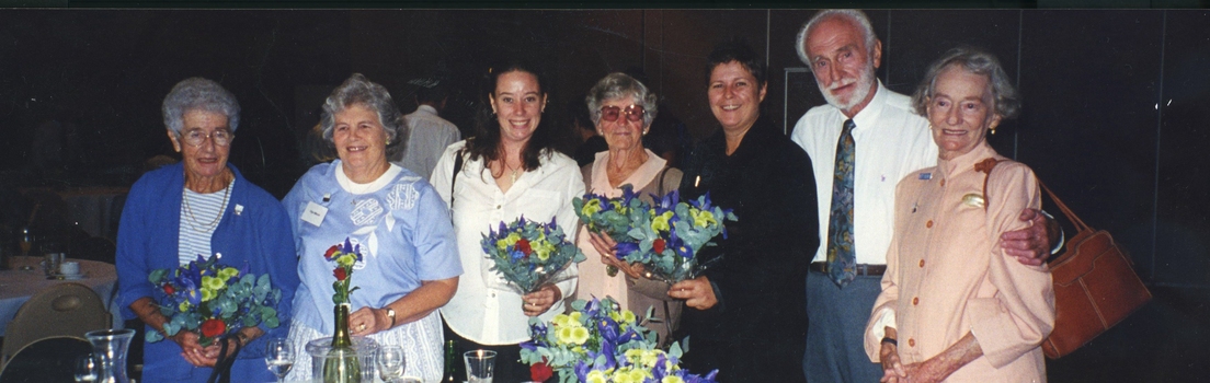 Six women and one man stand and smile for the camera at a function