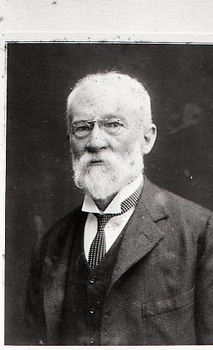 White haired older man wearing wire glasses looks to camera