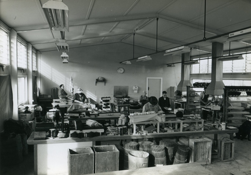Men stand at workstations working on various types of brushes
