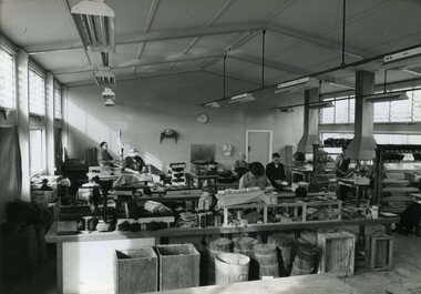 Men stand at workstations working on various types of brushes
