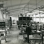 Men stand at workstations working on various types of brushes