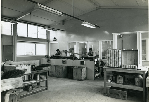 Men stand at workstations working on various types of brushes