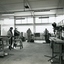 Men stand at workstations working on various types of brushes