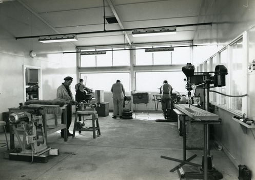 Men stand at workstations working on various types of brushes