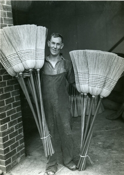 Male holds two different lengths of millet brooms in a doorway