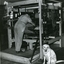 George Stibbs operating a mat making machine with Rex on lookout