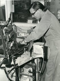 Man standing over machine that puts bristles into broom heads
