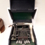 Open black box with metal typewriter which has seven keys and a small reel of paper