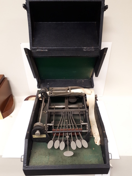 Open black box with metal typewriter which has seven keys and a small reel of paper