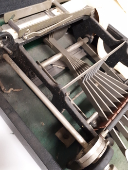 Open black box with metal typewriter which has seven keys and a small reel of paper