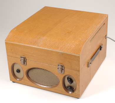 Wooden box with metal grill in front and two clasps.  To the side is a leather strap handle.