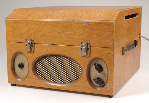 Wooden box with metal grill in front and two clasps.  To the side is a leather strap handle.