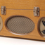 Wooden box with metal grill in front and two clasps.  Two plastic handles and an input connection sit either side of the grill.