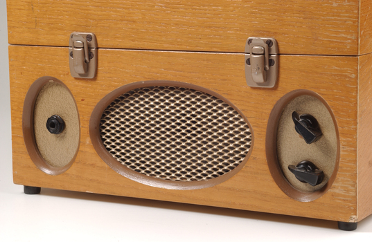 Wooden box with metal grill in front and two clasps.  Two plastic handles and an input connection sit either side of the grill.