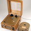 Wooden box with metal grill in front and two clasps.  A golden cartridge sits beside the player.