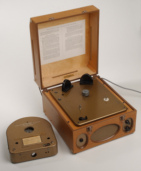 Wooden box with metal grill in front and two clasps.  A golden cartridge sits beside the player.