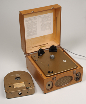 Wooden box with metal grill in front and two clasps.  A golden cartridge sits beside the player.