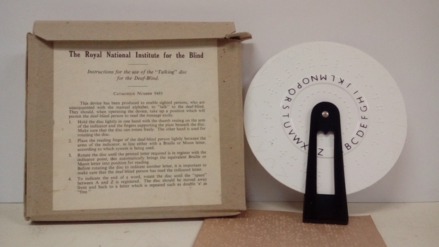 Cardboard box stands next to round wheel with Braille, held by a black plastic handle