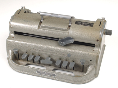 Metal Braille writer with nine grey keys, carriage return key and paper rollers on either side
