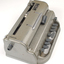 Metal Braille writer with nine grey keys, carriage return key and paper rollers on either side