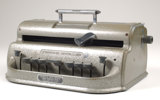 Metal Braille writer with nine grey keys, carriage return key and paper rollers on either side