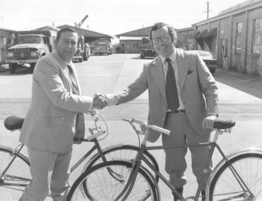 Two men shake hands whilst holding a Mitchell bicycle