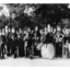 11 members of brass band in matching uniforms with instruments and 1 man beside picket fence