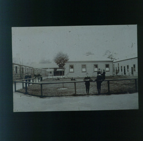 Boys and men standing behind or by a fence bordering a grassed area