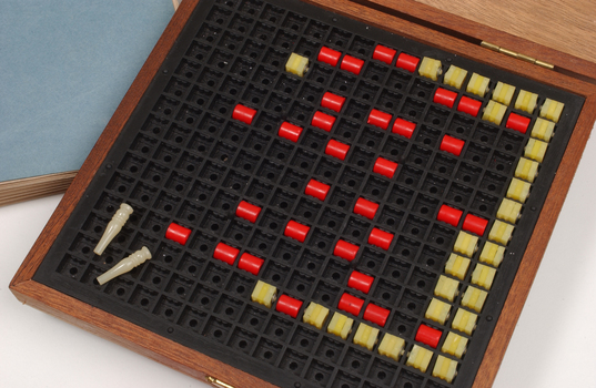 Braille book and wooden box containing yellow and red rubber markers that fit into the grid inset in the box