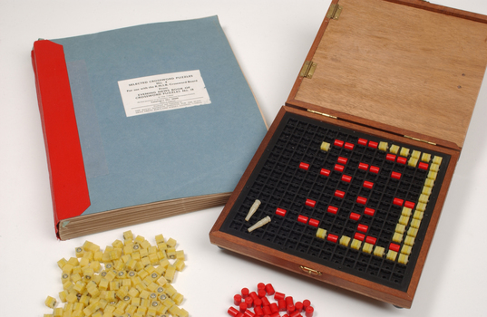 Braille book and wooden box containing yellow and red rubber markers that fit into the grid inset in the box