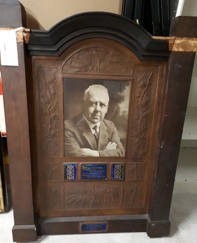 Brown wooden memorial tablet with inset of copper and photograph.