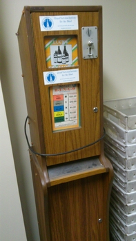 Chipboard rectangle with wooden veneer.  Metal covers for money slots and plastic covers over paper labels.