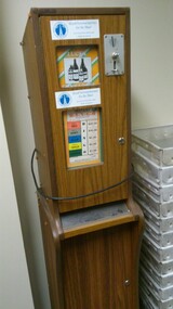 Chipboard rectangle with wooden veneer.  Metal covers for money slots and plastic covers over paper labels.
