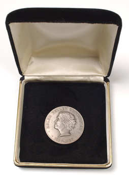 Silver coin with profile of short-haired woman turned to the left inside velvet box