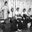 Five adults sit on chairs facing 5 school girls