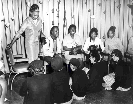 Five adults sit on chairs facing 5 school girls