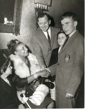 Seated woman shakes hand with schoolboy, whilst two school girls and a teacher look on