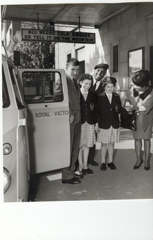 Three school children on pavement outside theatre with two cast members and RVIB combi beside them