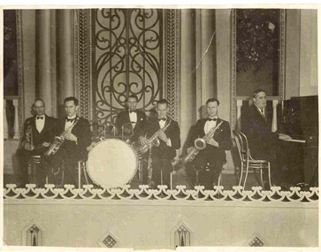 Six men sit on a stage with various instruments.